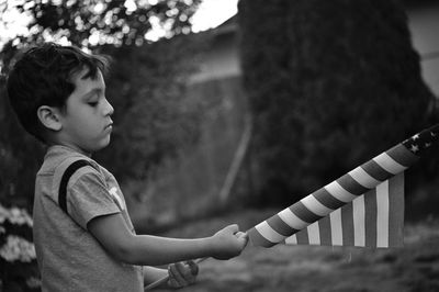 Side view of boy holding american flag while standing in yard