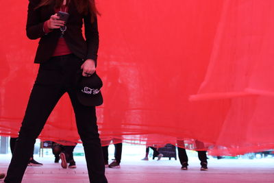 Midsection of woman using mobile phone while standing against red curtain