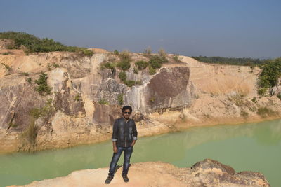 Portrait of young man standing on rock formation against sky