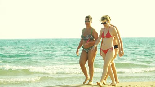 Friends standing on beach against clear sky