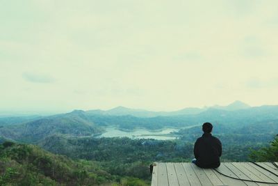 Rear view of man looking at mountain while sitting on observation point against sky