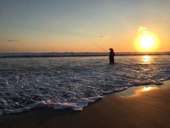 Silhouette man fishing in sea against sky during sunset