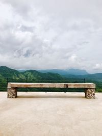 Empty bench against mountain range against sky