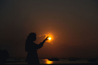 Rear view of woman photographing against sky during sunset