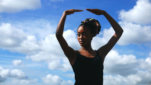 Young woman with arms raised standing against sky