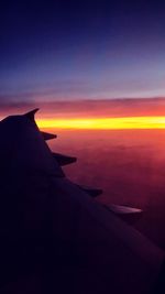 View of airplane wing over clouds during sunset