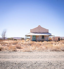 Abandoned building on field against clear blue sky