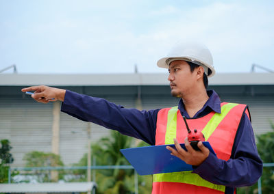 Engineer with clipboard and walkie-talkie gesturing at site
