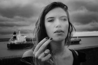Portrait of young woman smoking cigarette against sea