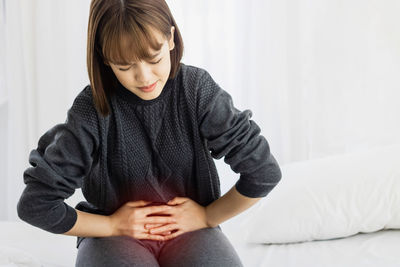 Woman with stomachache sitting on bed at home