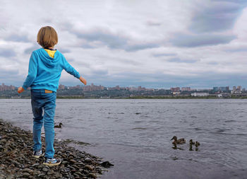 Rear view of boy standing by sea shore looking at water birds