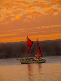 Sailboat sailing on sea against orange sky