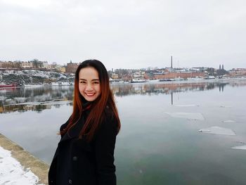 Portrait of smiling woman standing by lake in city