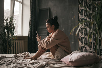 Side view of man using mobile phone while sitting on bed