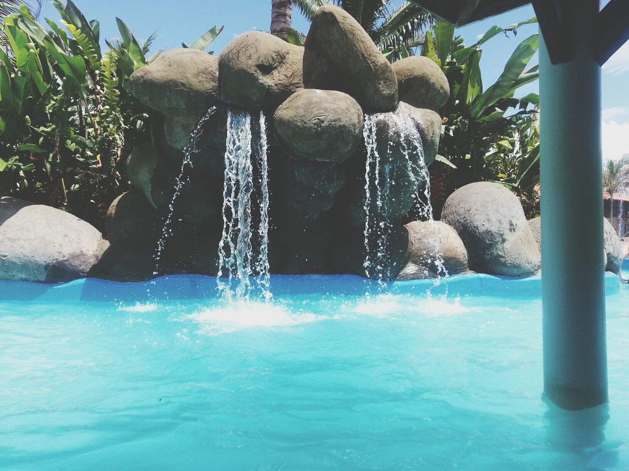 water, blue, waterfront, swimming pool, sea, nature, fountain, day, beauty in nature, outdoors, rock - object, tree, sunlight, tranquility, turquoise colored, no people, rippled, splashing, built structure, reflection