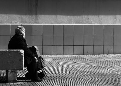 Rear view of woman sitting on bench against wall