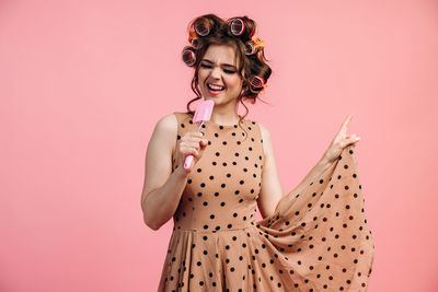 Young woman holding umbrella against pink background