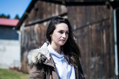 Young woman standing against warehouse during sunny day