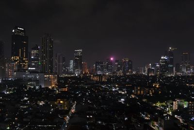 Illuminated modern buildings in city against sky at night