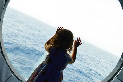 Girl looking through window against sea