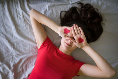 High angle view of young woman with heart shape on hands lying at bedroom