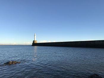 Lighthouse by sea against clear sky