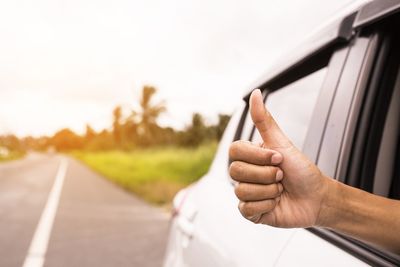 Midsection of man holding car on road against sky