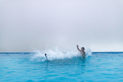 Young man splashing water in infinity pool