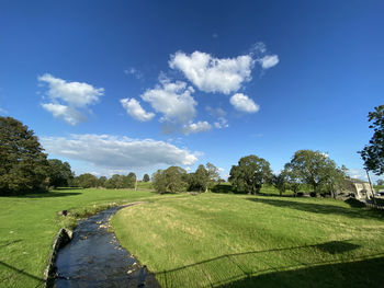 Late evening shadows, with a stream, meadow, houses, and trees in, long preston, skipton, uk