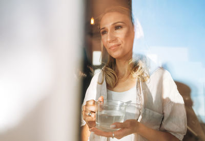 Young adult woman blonde long hair with glass of water on morning kitchen at home, healthy lifestyle