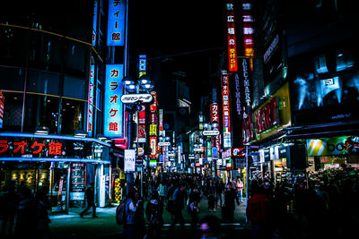 People on street amidst illuminated billboards on buildings in city