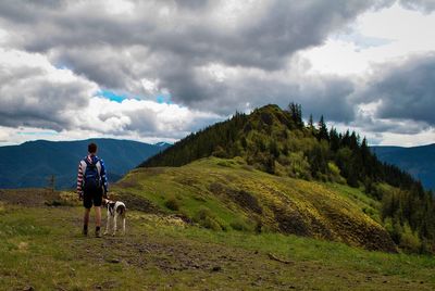 Man with dog standing on mountain against sky