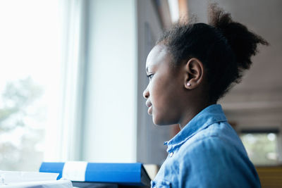 Close-up of thoughtful girl looking through window in classroom