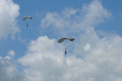 Low angle view of people paragliding against cloudy sky