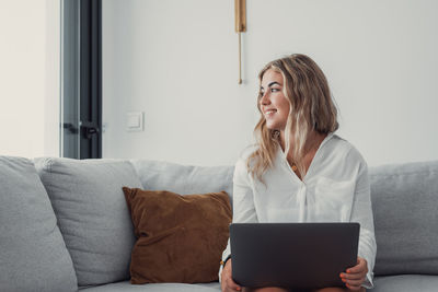 Young woman using laptop while sitting on sofa at home