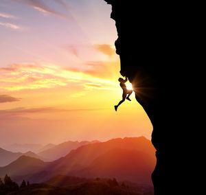 Silhouette man climbing mountain against cloudy sky during sunset