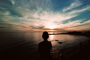 Silhouette of person on beach against cloudy sky at sunset