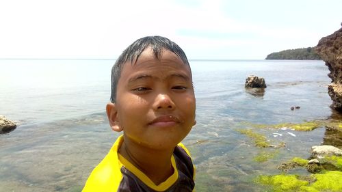 Portrait of teenage boy at beach against sky