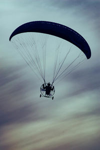 Low angle view of silhouette person paragliding against sky