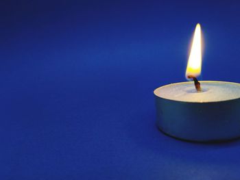 Close-up of illuminated tea light on blue background