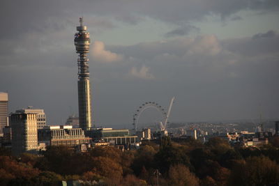 Communications tower in city against cloudy sky