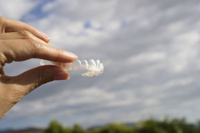 Cropped hands of person holding dentures against sky