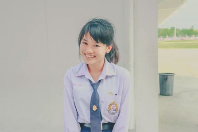 Portrait of smiling young woman in uniform standing against wall