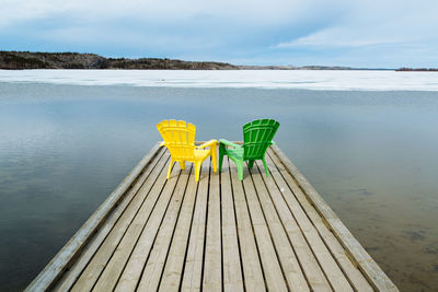 Green and yellow adirondack chairs on pier at lake during winter