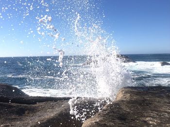 Sea waves splashing on rocks against clear sky