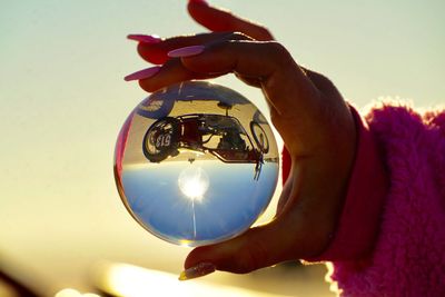 Cropped hand holding crystal ball with reflection of motorcycle during sunset