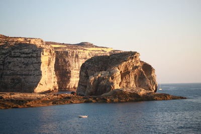 Rock formations by sea against clear sky