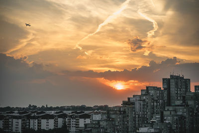 Buildings in city against dramatic sky during sunset