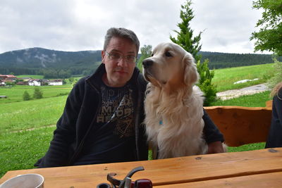 Portrait of man with dog on bench against landscape