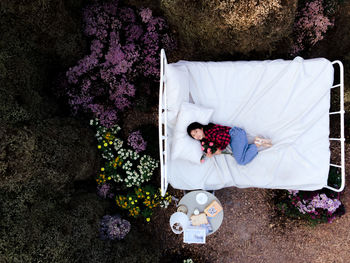 Drone shot of girl lying on bed amidst trees in forest